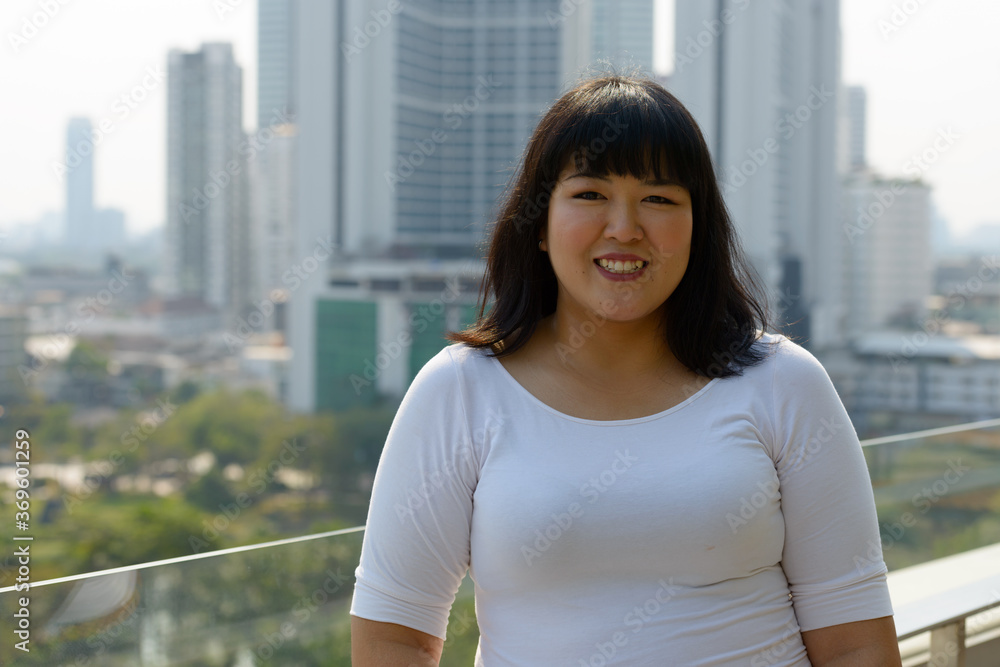 Happy young beautiful overweight Asian woman against view of the city