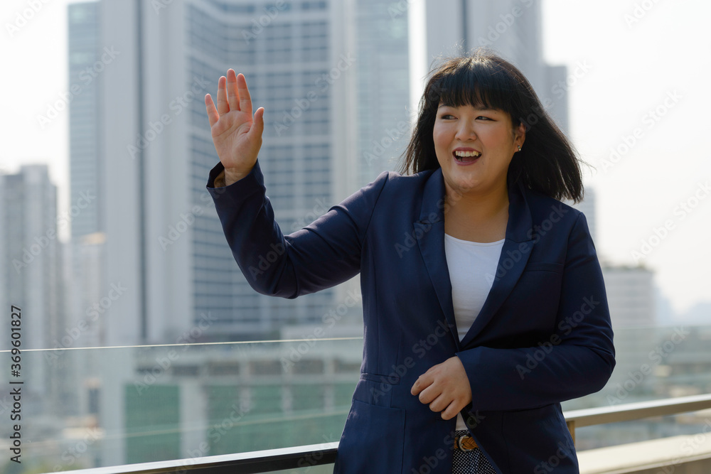 Happy young beautiful overweight Asian businesswoman against view of the city