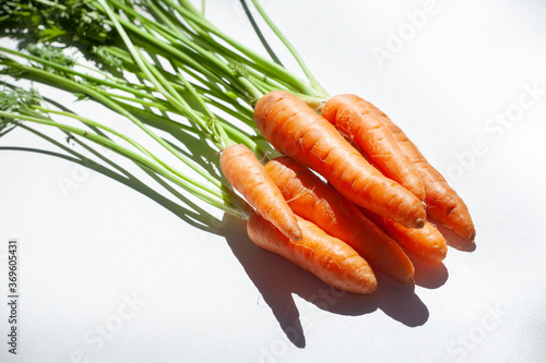 Group of carrots in perspective, raw with stems and leaves on light background
