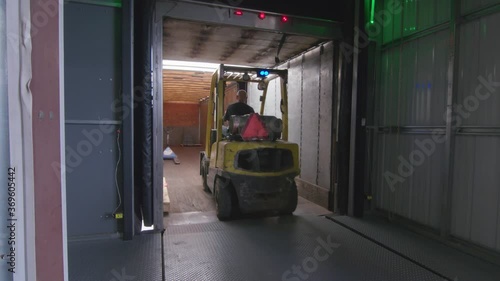 Worker on Forklift loads truck trailer with gear pallets in shipping bay dock