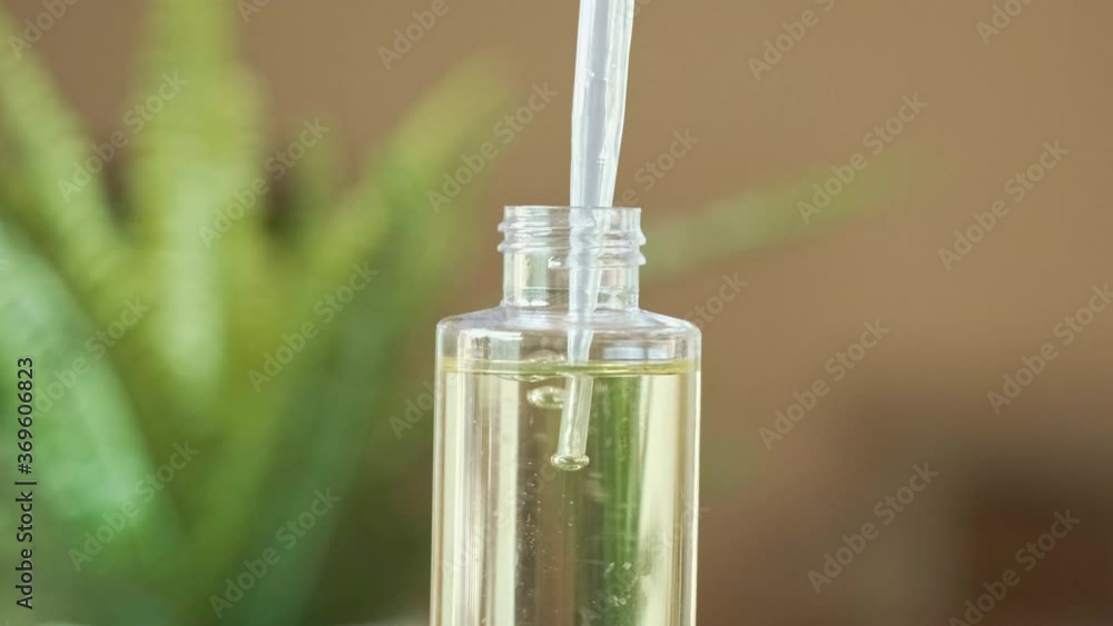 Slow Motion Essential Oil Dropper Squeezing Droplets of Oil back into Clear Container, Soft Fern in Background, Bright and Fresh, Spa Day Slow Motion Essential Oil Dropper Squeezing Droplets of Oil back into Clear Container, Soft Fern in Background, Bright and Fresh, Spa Day