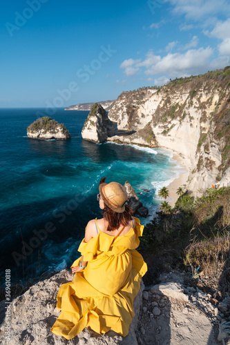 Wallpaper Mural Young happy woman traveller sitting on top of cliff and looking to Diamond beach in a morning sunrise. A woman enjoying summer season outdoor lifestyle. Nusa Penida near Bali island, Indonesia Torontodigital.ca