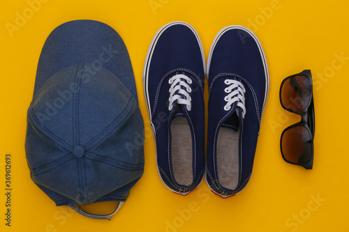 Cap and sunglasses, sneakers on yellow background. Top view. Flat lay