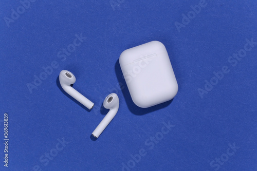 White true wireless bluetooth headphones or earbuds with charging case on blue background. Top view. Flat lay