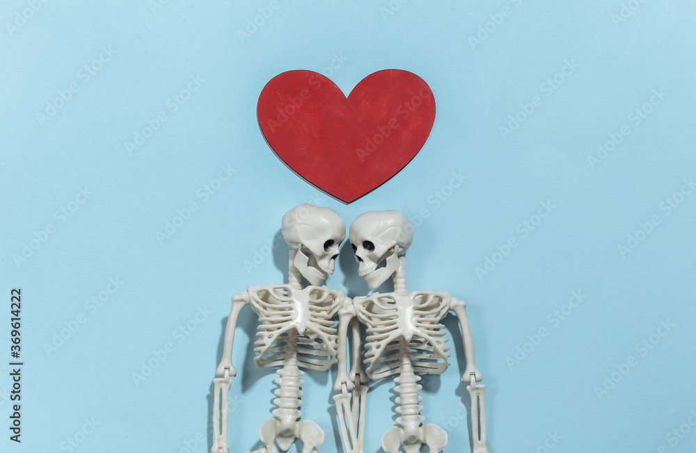 Couple of lovers skeletons and red decorative heart on a bright blue background. Valentine's day or halloween theme. Top view. Flat lay Couple of lovers skeletons and red decorative heart on a bright blue background. Valentine's day or halloween theme. Top view. Flat lay