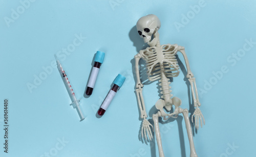 Skeleton, syringe and test tubes with blood on a blue background. Top view