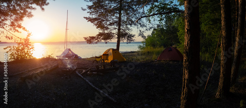 Panorama of the campground with two hiking tents set on the area and one sailing catamaran beached on the coast. photo