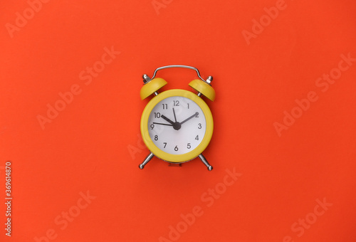 Yellow retro alarm clock on orange bright background. Top view. Minimalism