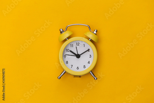 Yellow retro alarm clock on a yellow background. Top view. Minimalism