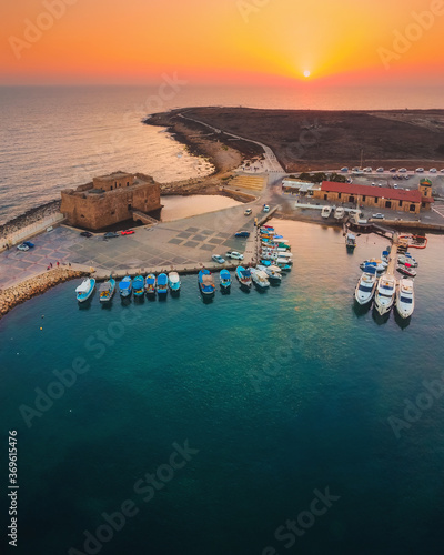 Beautiful aerial sunset shot of Paphos Castle and Paphos Harbor in Cyprus. Crystal clear water, fishing boats, luxury yachts - amazing travel destination for all year vacation. 