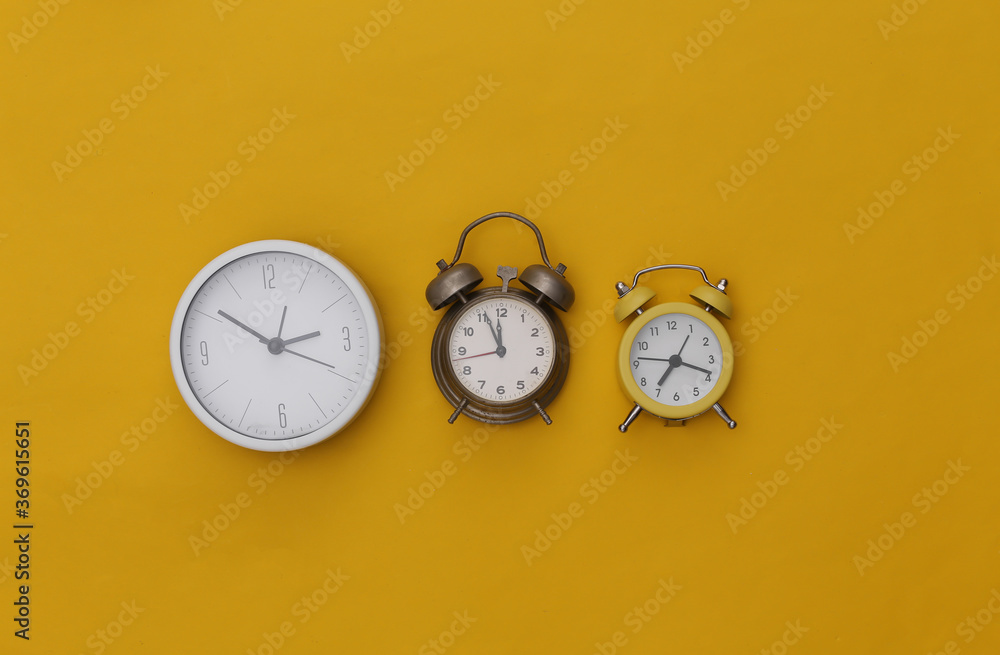 Three alarm clocks on yellow background. Top view. Flat lay Three alarm clocks on yellow background. Top view. Flat lay