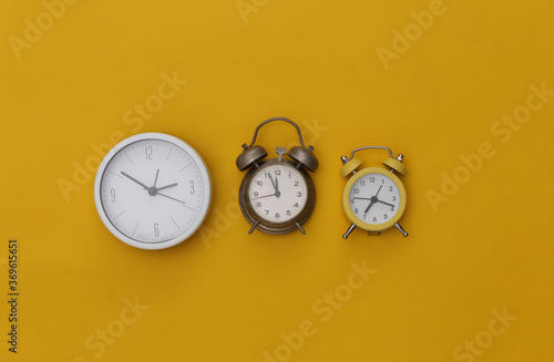 Three alarm clocks on yellow background. Top view. Flat lay