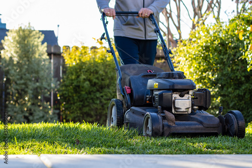 Middle Aged man mowing the lawn with a self-propelled lawn mower on a sunny winter afternoon.