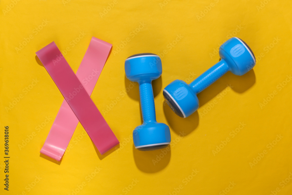 Fitness elastic bands and dumbbells against yellow bright background with deep shadow. Top view. Flat lay Fitness elastic bands and dumbbells against yellow bright background with deep shadow. Top view. Flat lay