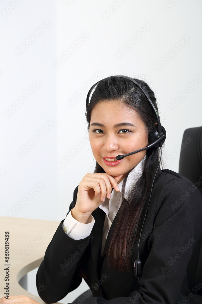 Young Asian female wearing suit sitting at office desk look at camera headphone call center Young Asian female wearing suit sitting at office desk look at camera headphone call center