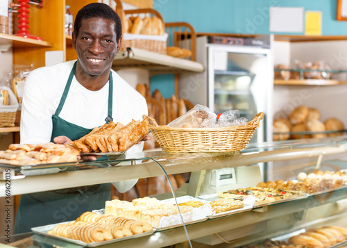 Fine African American man working in small bakery, offering appetizing freshly baked bread and pastry