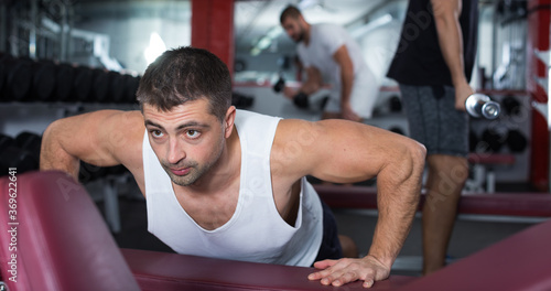 Strong sporty man doing push-ups on bench during workout in gym