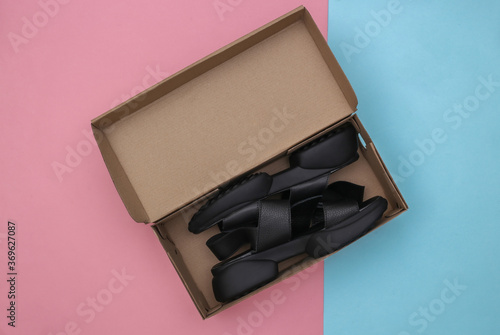 New leather sandals in packing box on blue-pink pastel background. Top view
