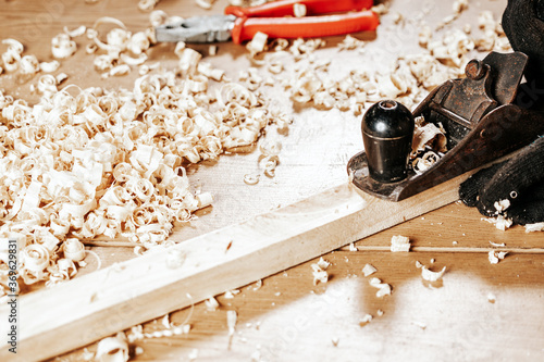 Close up of the a young brunette man builder handles a wooden bar with a black jack plane in the workshop, in the background a lot of wooden boards and tools