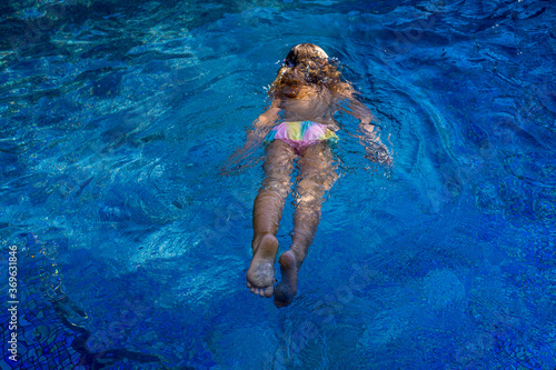 Little girl swims in the blue swimming pool. Hight quality photo