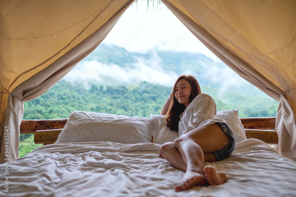 Portrait image of a young woman lying on a white bed in the morning with a beautiful nature view outside the tent
