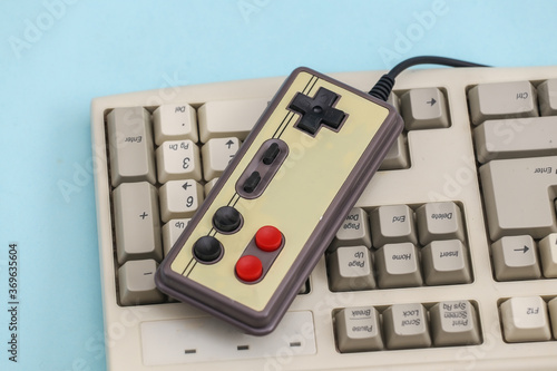 Retro gamepad on old pc keyboard. Blue background. Attributes 80s, gaming photo