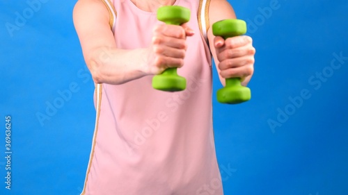 Female in a pink sports suit with dumbbells in hands does exercises on a blue background. The concept of sports, diet and weight loss.