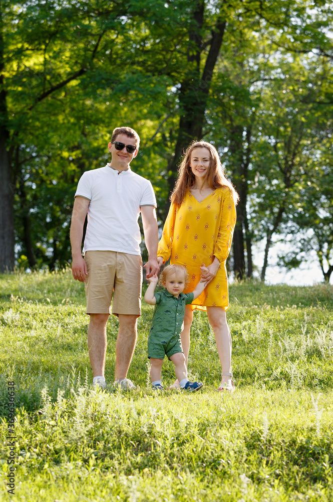 Family life. Portrait of parents and their son on the background of nature. Walk in park. Happy family leisure outdoors.