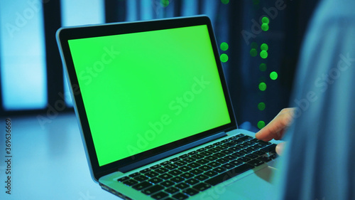 Wallpaper Mural Close-up IT admin holding a mock-up chroma key green laptop at server racks. Engineer with notebook monitoring an operationa server cabinet in futuristic data center. Torontodigital.ca