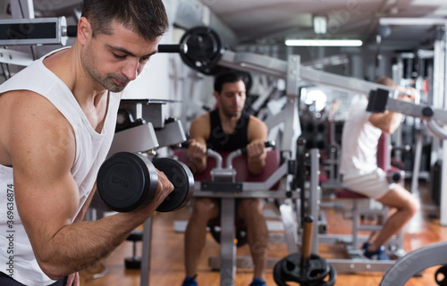 Concentrated sporty guy during workout in gym with dumbbells