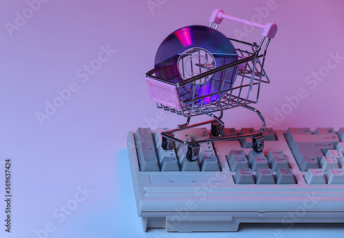 Shopping trolley with CD on old pc keyboard. Pink blue gradient neon, holographic light. Retro Attributes 80s
