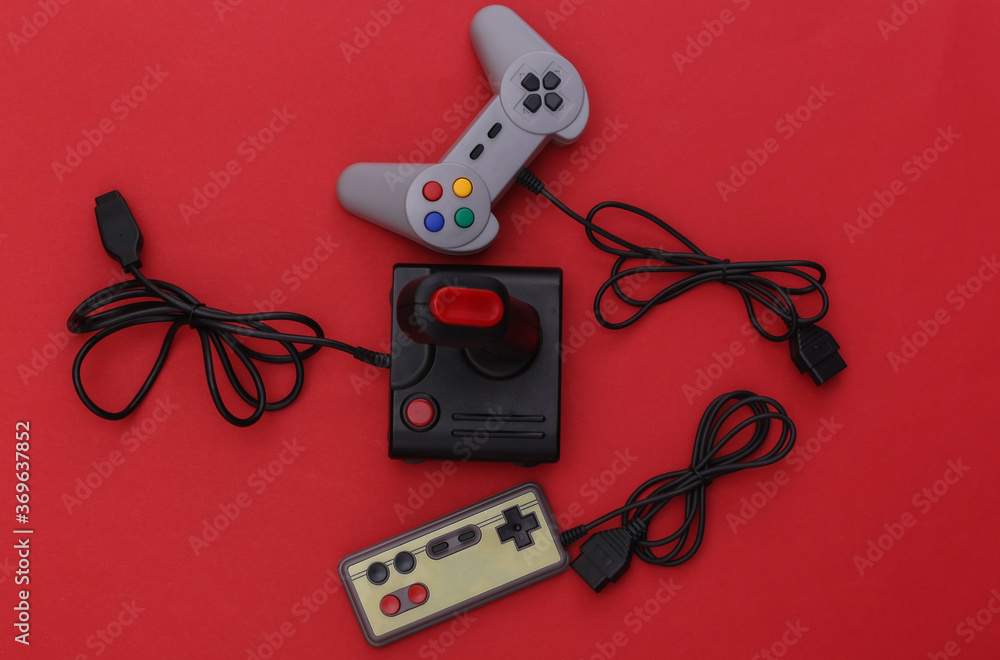 Wired retro gamepads and joystick with wound cable on red background. Video game, gaming. Top view Wired retro gamepads and joystick with wound cable on red background. Video game, gaming. Top view
