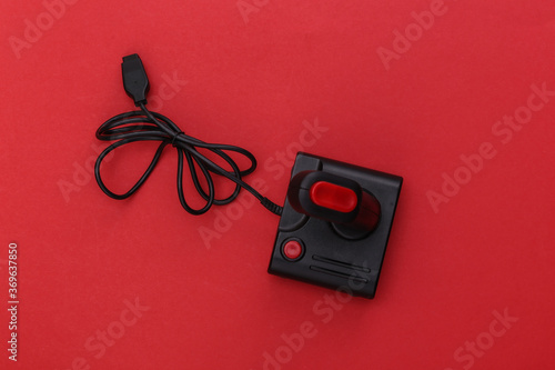 Wired retro joystick with wound cable on red background. Video game, gaming. Top view