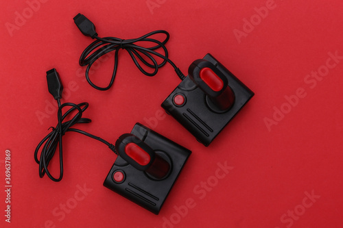 Two wired retro joysticks with wound cable on red background. Video game, gaming. Top view