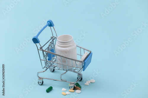Shopping trolley with pills bottle on a blue background.