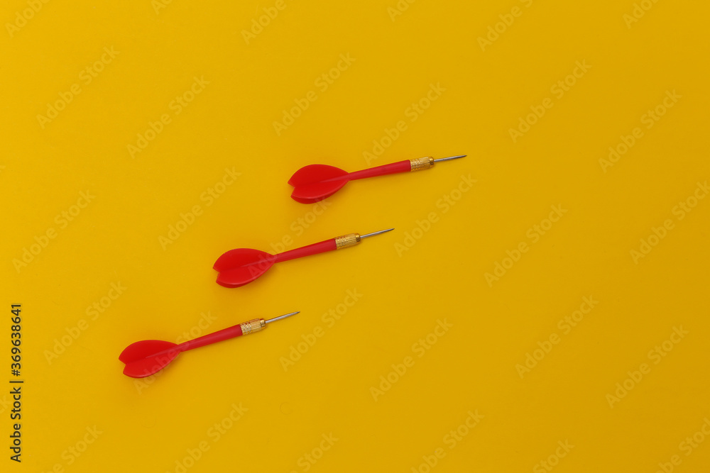Three red plastic darts with metal tip on yellow background. Top view. Flat lay Three red plastic darts with metal tip on yellow background. Top view. Flat lay