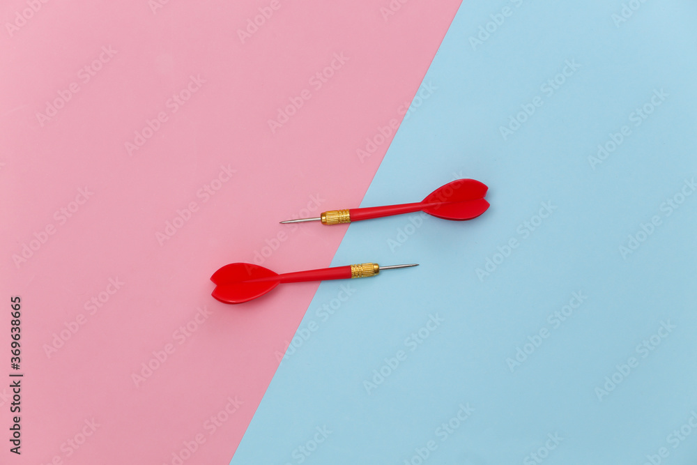 Two red plastic darts with metal tip on pink blue pastel background. Top view. Flat lay. Minimalism Two red plastic darts with metal tip on pink blue pastel background. Top view. Flat lay. Minimalism