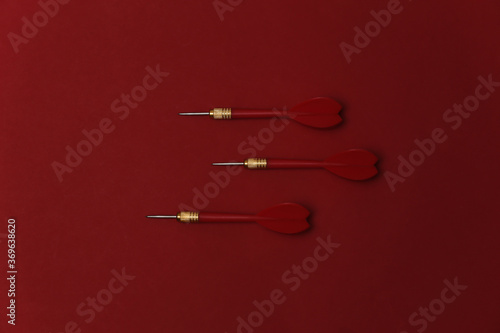 Three plastic darts with metal tip on red background. Top view. Flat lay