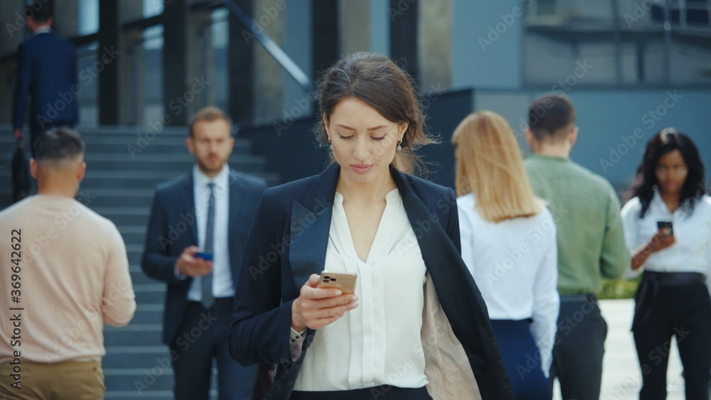 Appealing young caucasian businesswoman with smartphone walks in corporate neighbourhood outdoors. Business people lifestyle. Social distancin Technology. Appealing young caucasian businesswoman with smartphone walks in corporate neighbourhood outdoors. Business people lifestyle. Social distancin Technology.