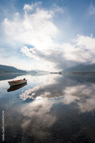 A boat on a flat mirror like lake with dramatic clouds in the mountains.  © Luke
