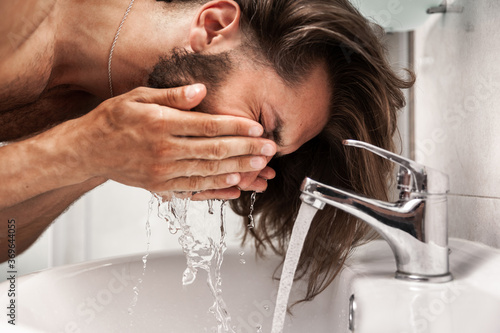 Man with long hair washes his face in the bathroom, close-up portrait
