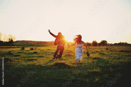 Lovely young couple are having fun and running outdoors in the field on summer day. romantic photo at sunset time. love story.