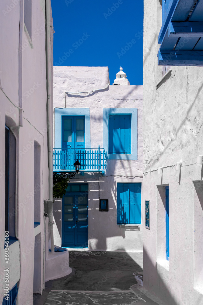 Portrait vertical view of Plaka Town street on Milos Island, Greece with no people. Traditional greek architecure with whitewashed houses and walls, and vivid blue door frames and window shutters. 