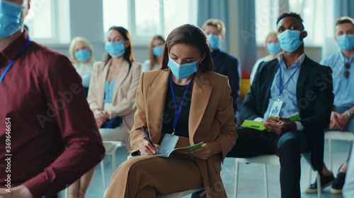 Businesswoman at meeting discussing start-up plan strategy with the speaker. Multi-ethnic corporate professionals in masks listening to business seminar on quarantine.