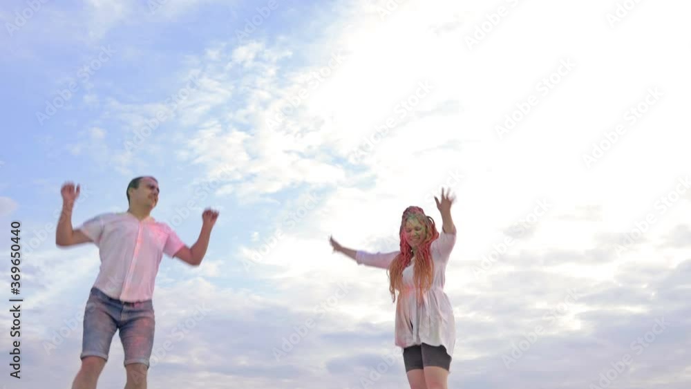 Cheerful couple is jumping on the top of a sandy hill. Clothes and faces are stained with Holi powder. Against the background of the sky. Cheerful couple is jumping on the top of a sandy hill. Clothes and faces are stained with Holi powder. Against the background of the sky.