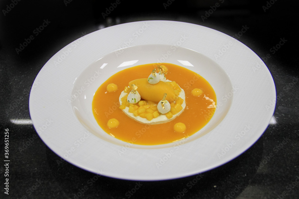 High cuisine dessert: Mango Ice cream with jelly mango fruit in a white meringue, on a black background. 45 degree view angle on a isolated ceramic white plate. High cuisine dessert: Mango Ice cream with jelly mango fruit in a white meringue, on a black background. 45 degree view angle on a isolated ceramic white plate.