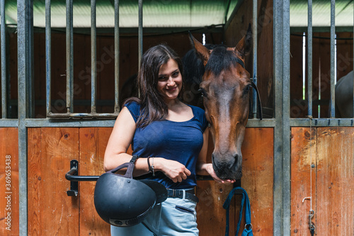 Portrait of a young woman with horse in the stable taking a break from exercises after a riding lesson - Millennial having fun with her animal friend in the summer