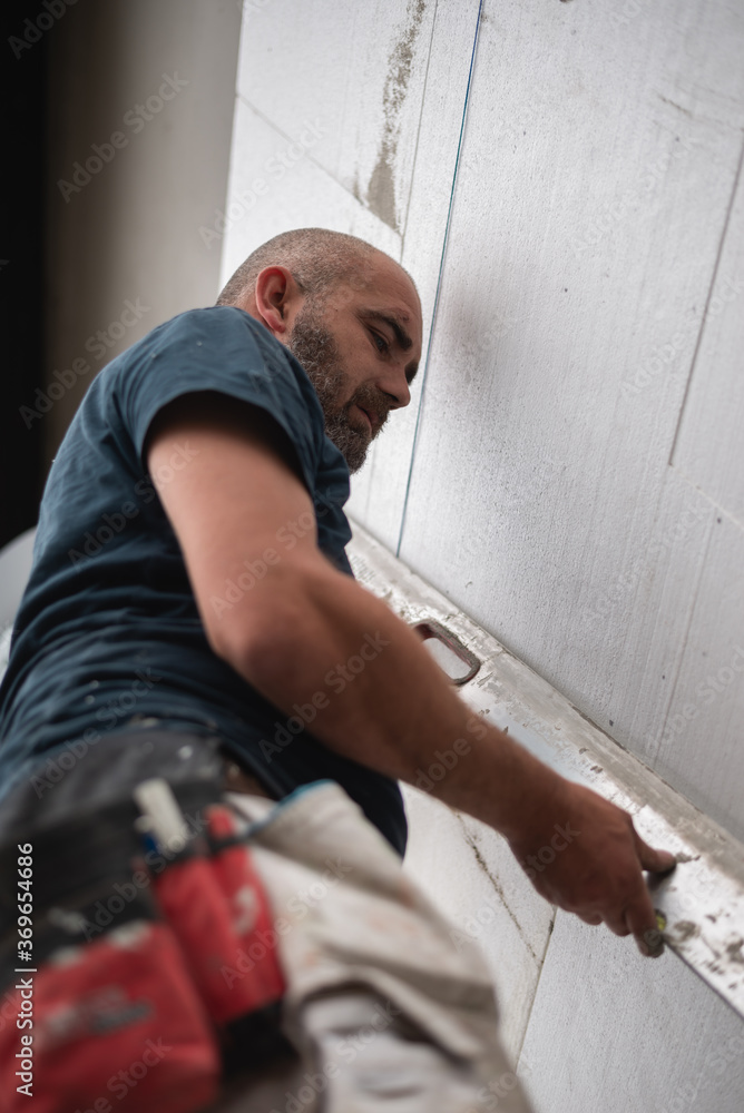 Construction worker working on a house facade checking level of glued boards Construction worker working on a house facade checking level of glued boards