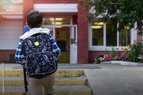 Child boy with bag go to elementary school. Back view