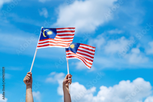 Hand happily waving Malaysia flag against blue sky. photo